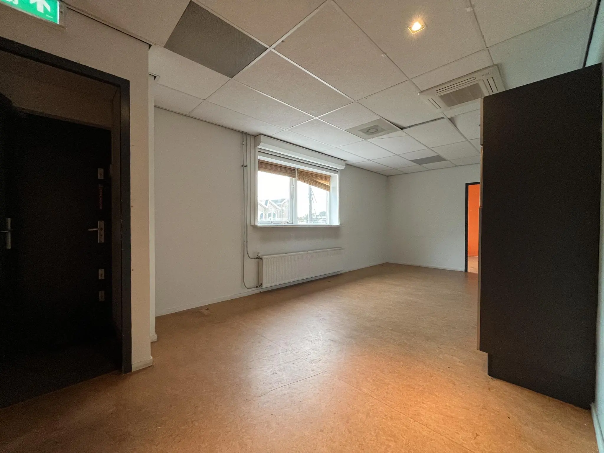 Leeg kantoorruimte aan de 2e Daalsedijk met systeemplafond, grote ramen en een open doorgang naar een naastgelegen kamer.